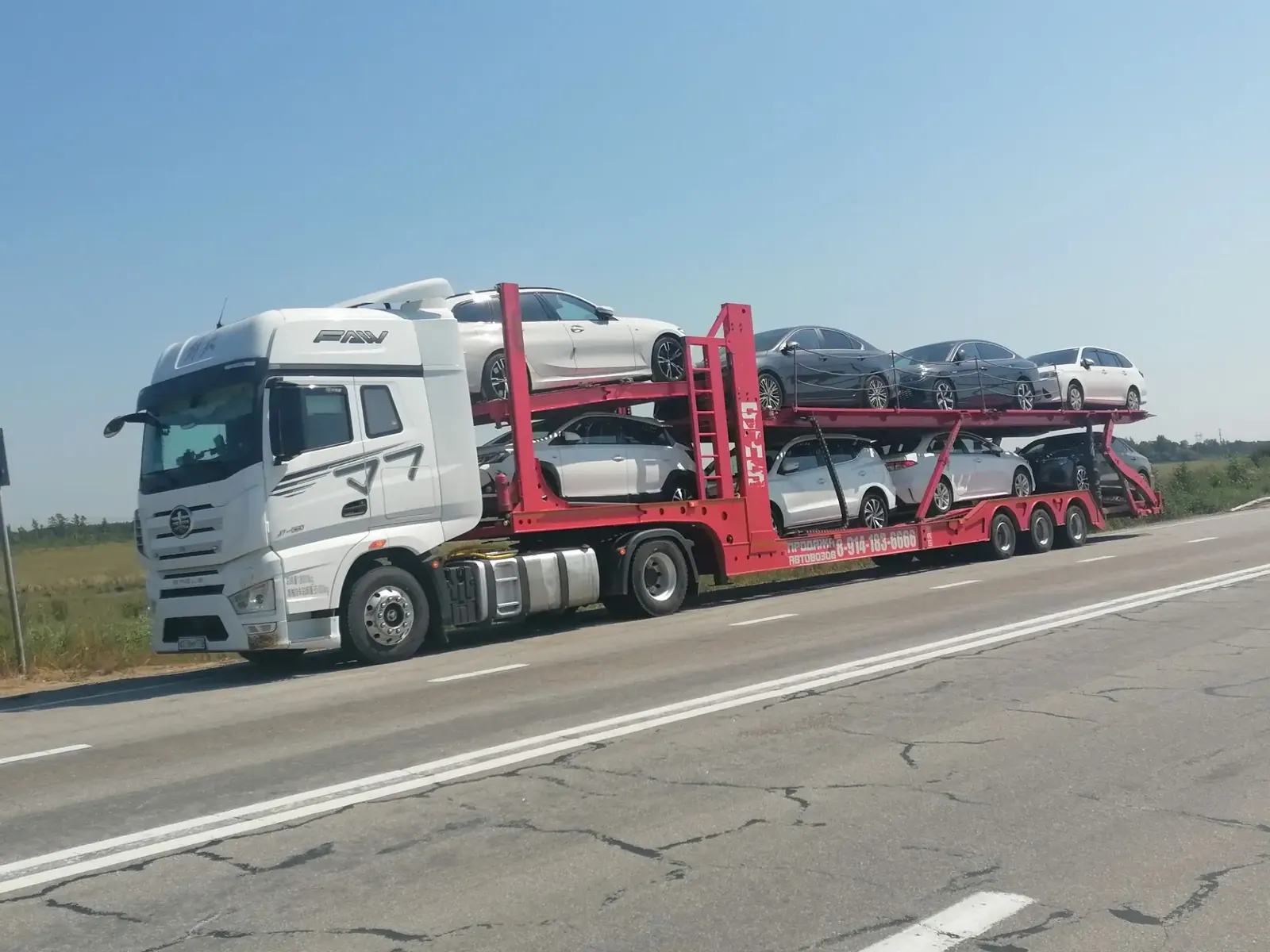 Автовоз FAW с автомобилями в дороге по трассе